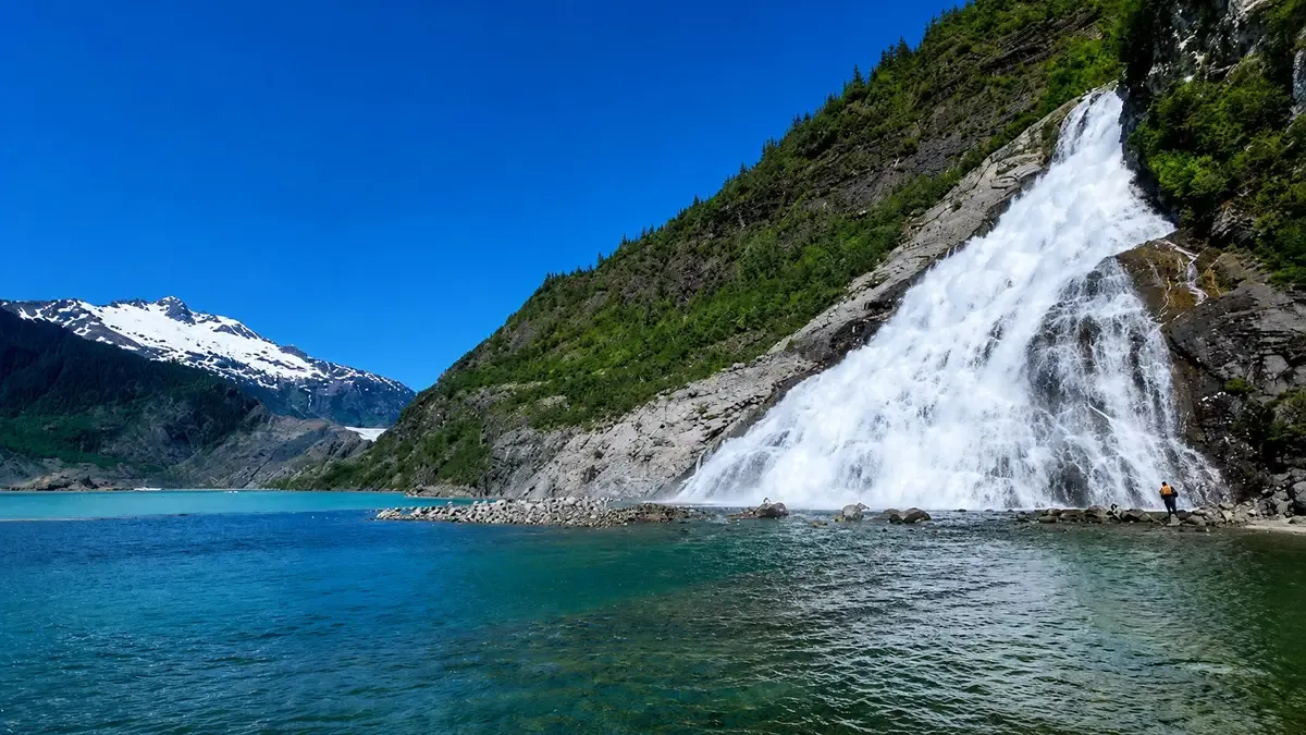 Hiker on the gravel trail approaching Nugget Falls beside Mendenhall Glacier on a Nugget Falls and whale watching tour with whale guarantee from Juneau