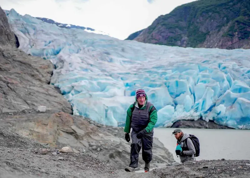 Guided group in rain gear approaching the blue ice face on a Mendenhall Glacier ice adventure canoe and hike tour