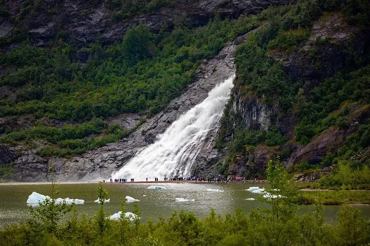 Nugget Falls thundering beside the blue ice face seen on Mendenhall Glacier tours from Juneau, Alaska