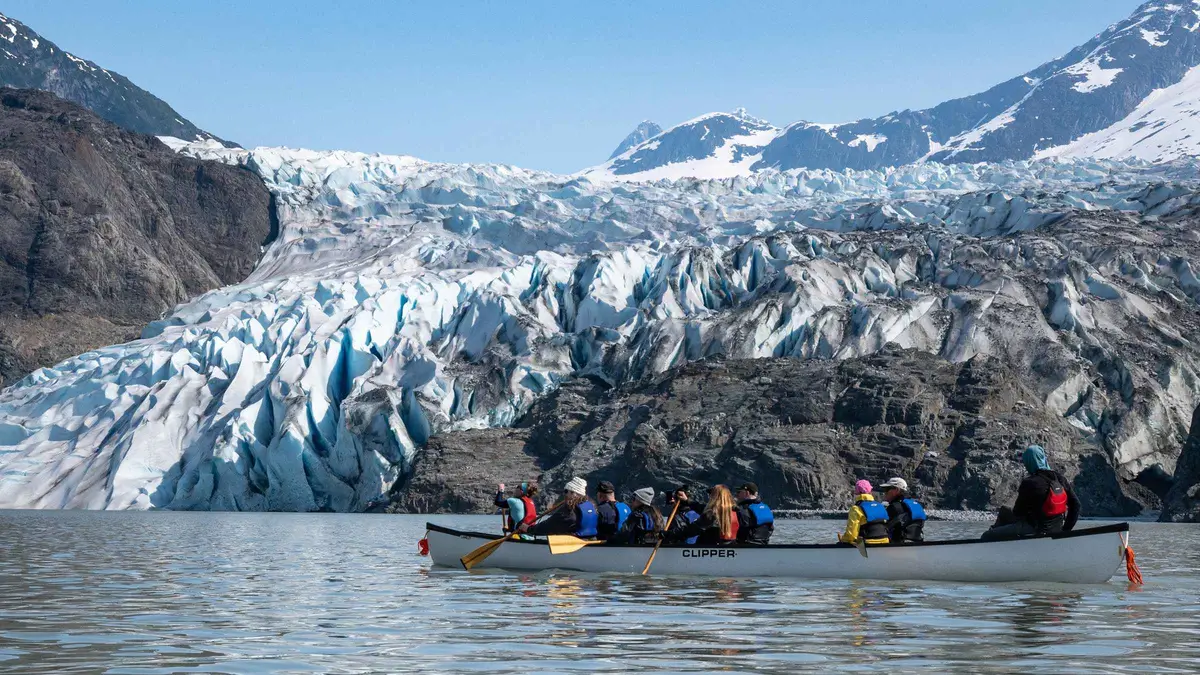 Paddlers landing their canoe on the moraine below the blue ice on a Mendenhall Glacier canoe paddle and hike tour